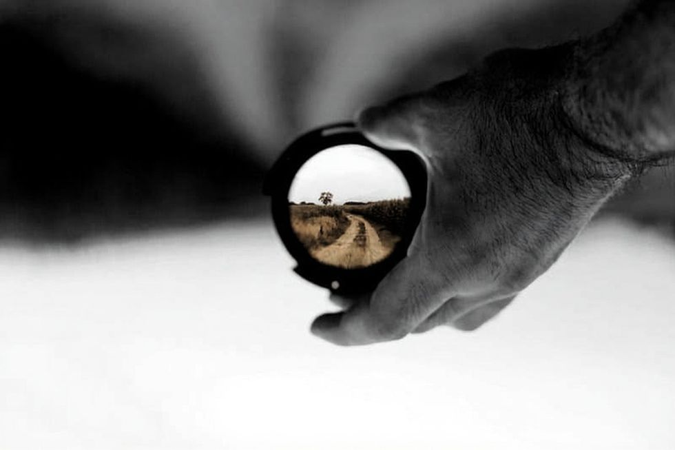 A hand holding a lens through which a country road comes into focus